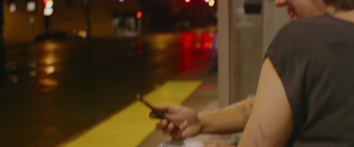 A man and woman look at a phone at a bus stop