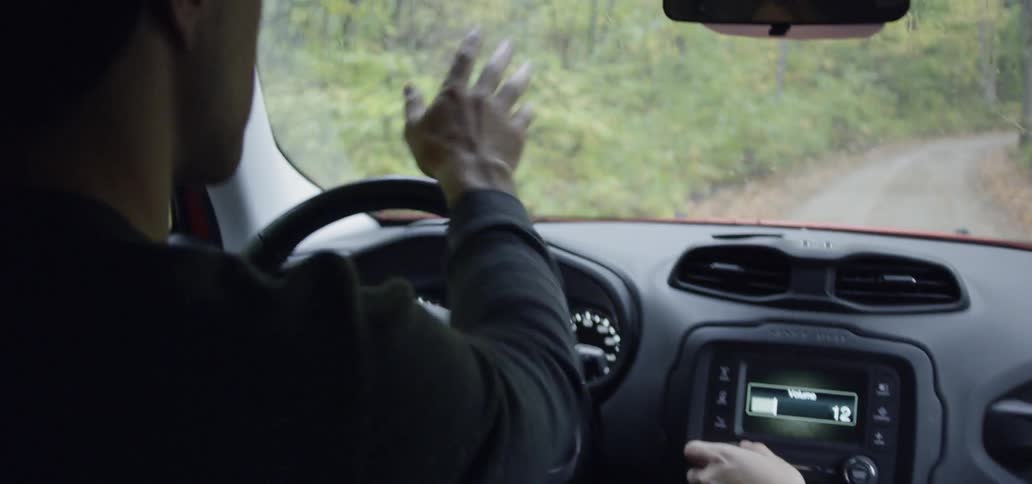 Man drives a car while a woman adjusts the radio