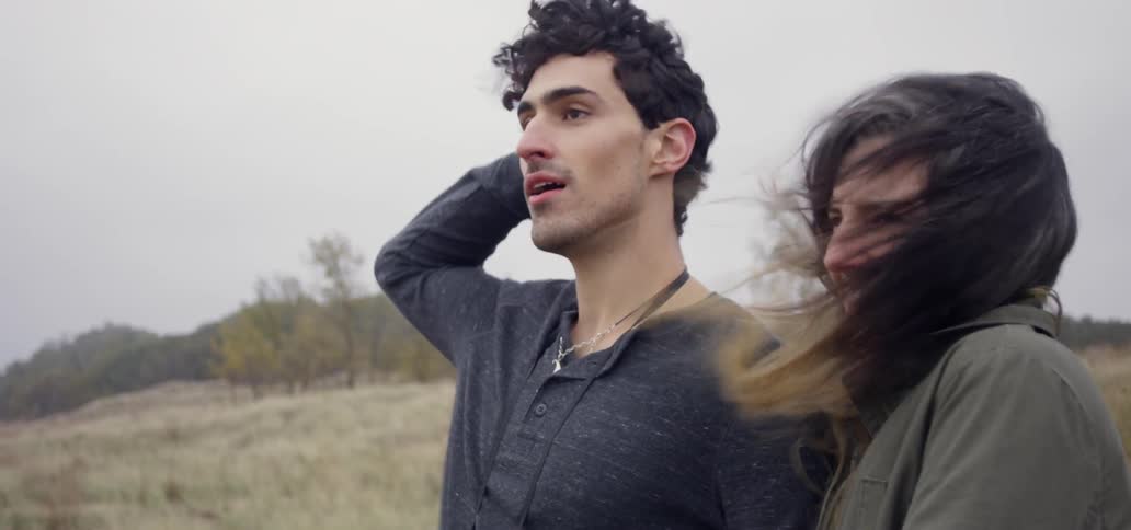 Man and woman walk through a field on a windy day