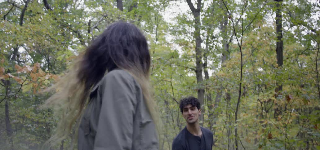 Man tosses a stone to a woman as they walk in the forest