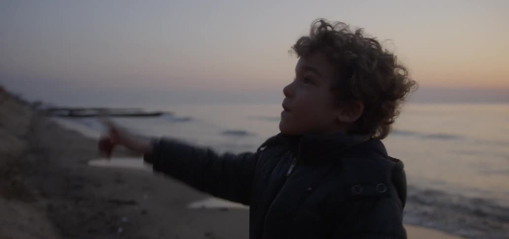 Child pointing upwards at the beach at sunset