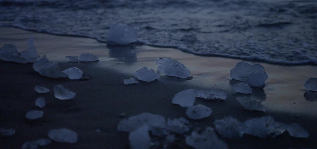Chunks of ice lay on the sand of a beach as the tide comes in at dusk