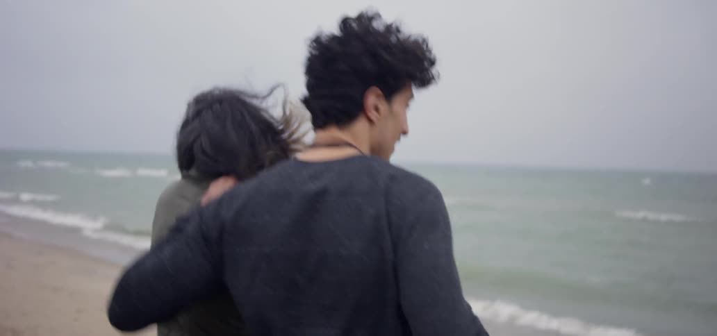 A couple stands on the beach as they wind blows their hair
