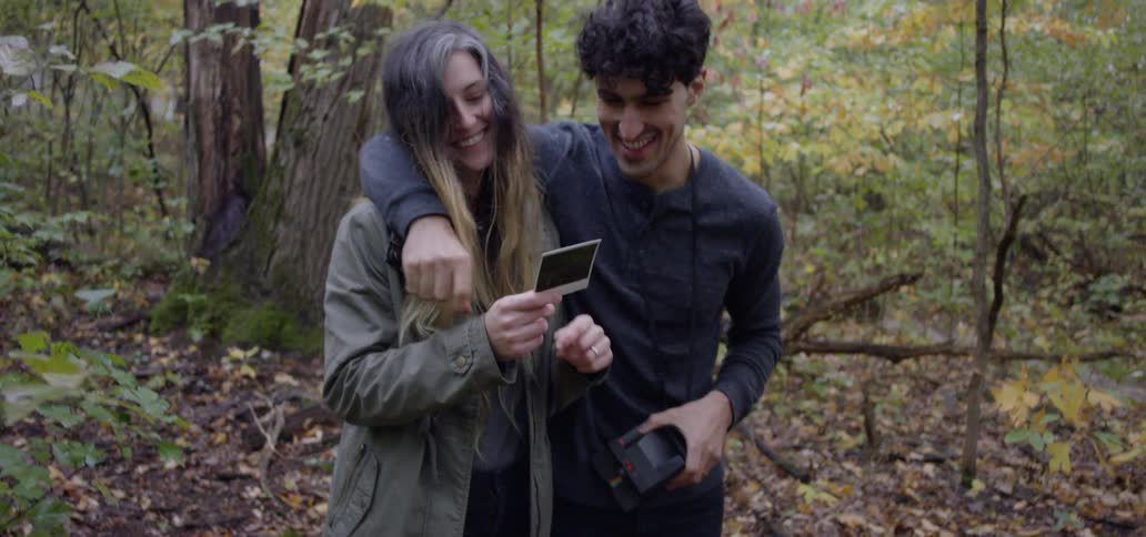 A man and woman look at a photograph in a forest