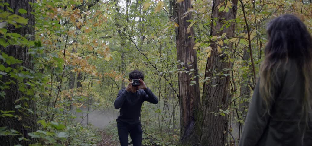 Man takes a photo of a woman while in a forest