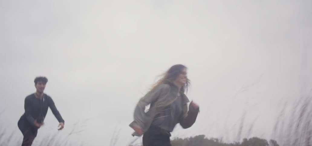 A man and woman run over sand and grass