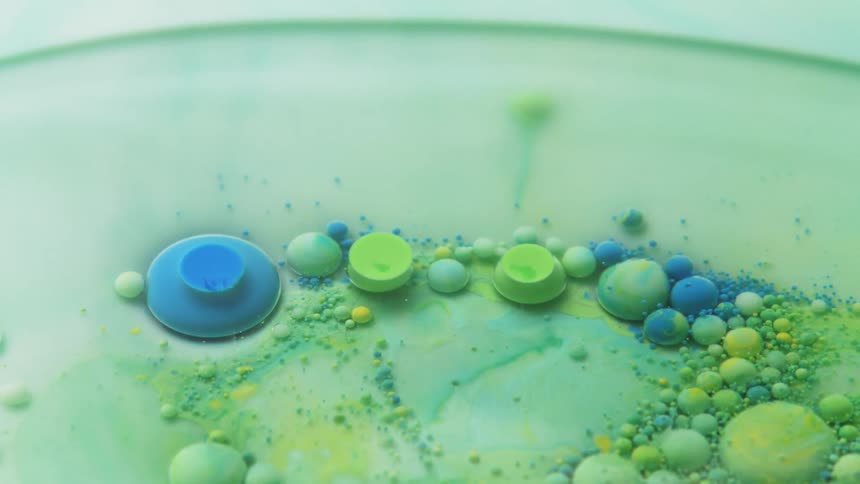 Blobs of blue green and yellow paint expand and float in liquid
