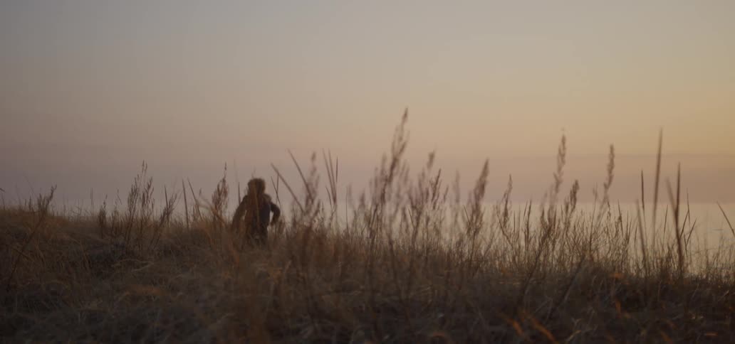 Boy runs through tall grass at sunset