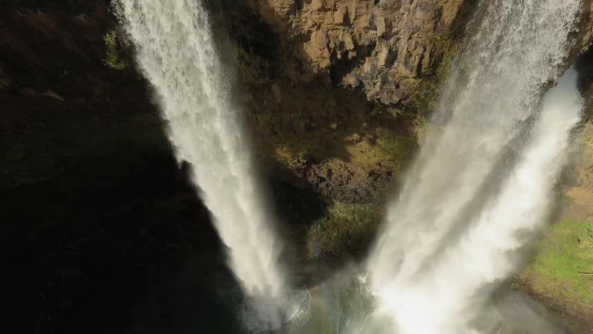 Cascading waterfalls are flowing over a cliff into a natural pool during the day