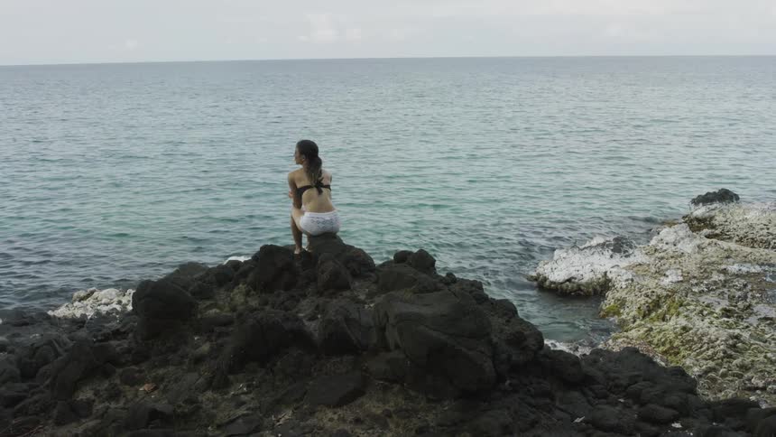Woman sits on a rock formation overlooking water