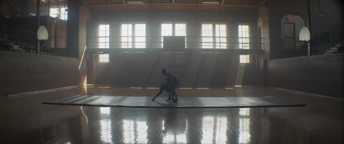 Two people wrestle on a large mat near the windows