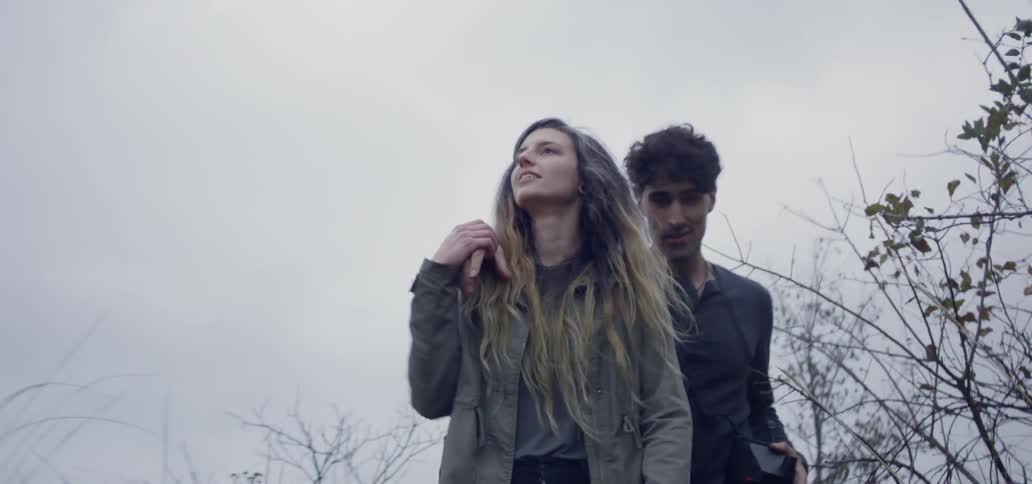 A man is putting his arm on a woman's shoulders as they walk on a cloudy day