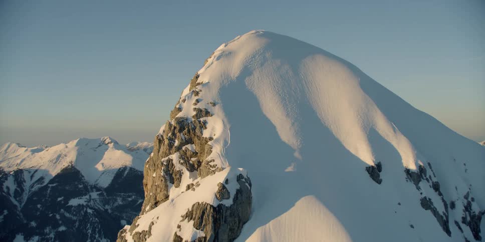A cross is standing on a high mountain peak in a mountain range during the day