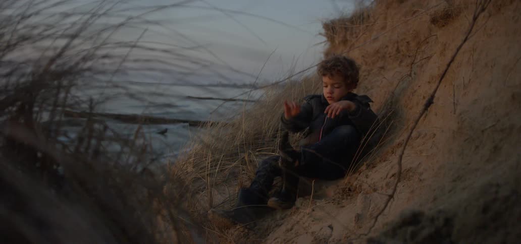 The child sits on the hill by the water