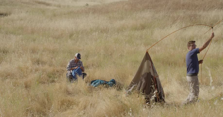 A man struggles to set up a tent then gives up while another watches