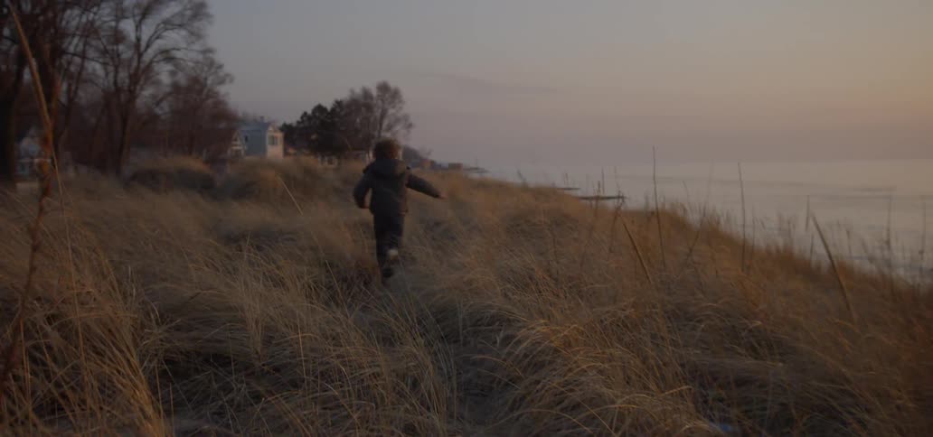 The child is running through the grass at sunset