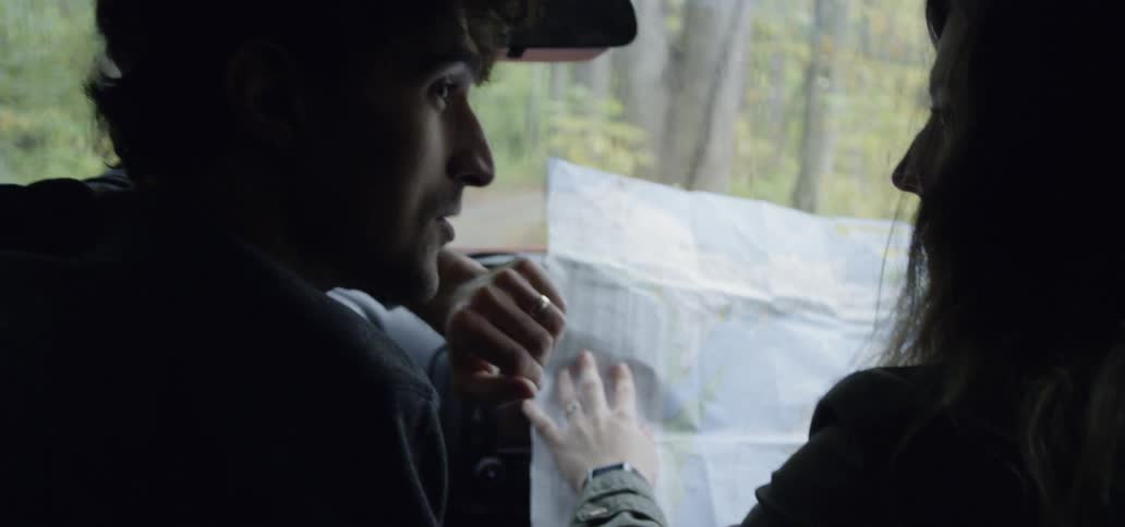 A man and a woman inside a car near a forest look at a large map