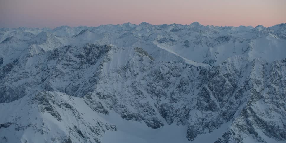The sun is setting behind the snow covered mountains
