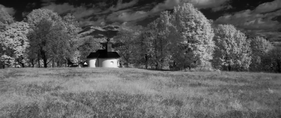 Small white building in the middle of a field surrounded by hills and trees