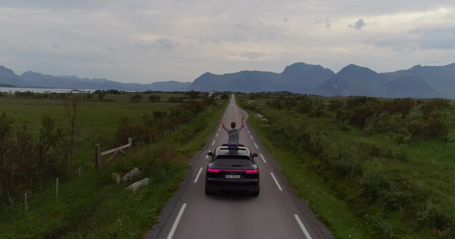 A man stands through an open moonroof while traveling on a rural road