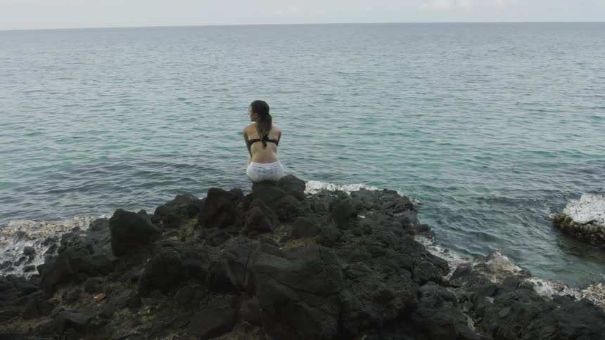 A woman sits on a pile of rocks on a beach