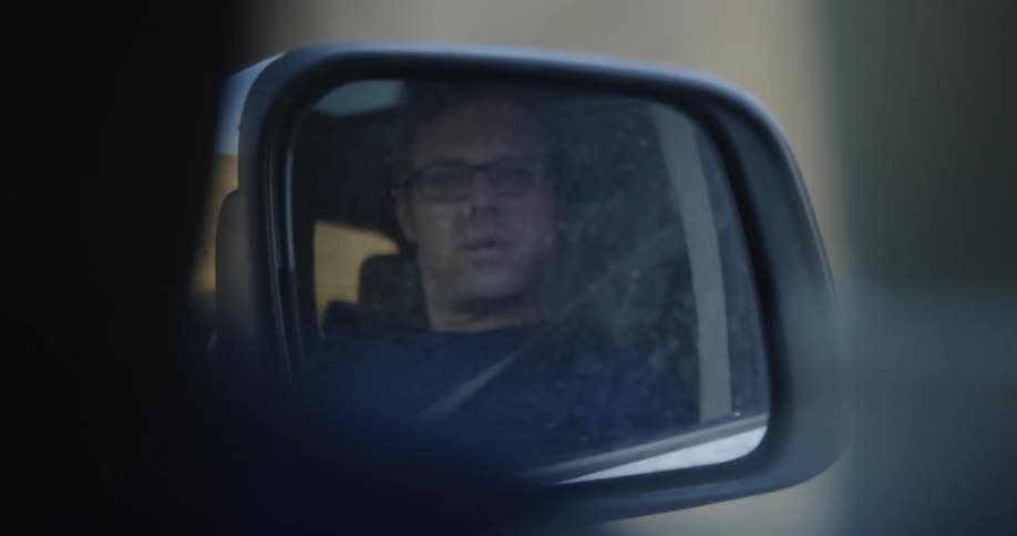 A man looks in a side mirror as he drives