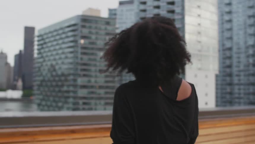 Woman walks on a balcony and looks over some city buildings