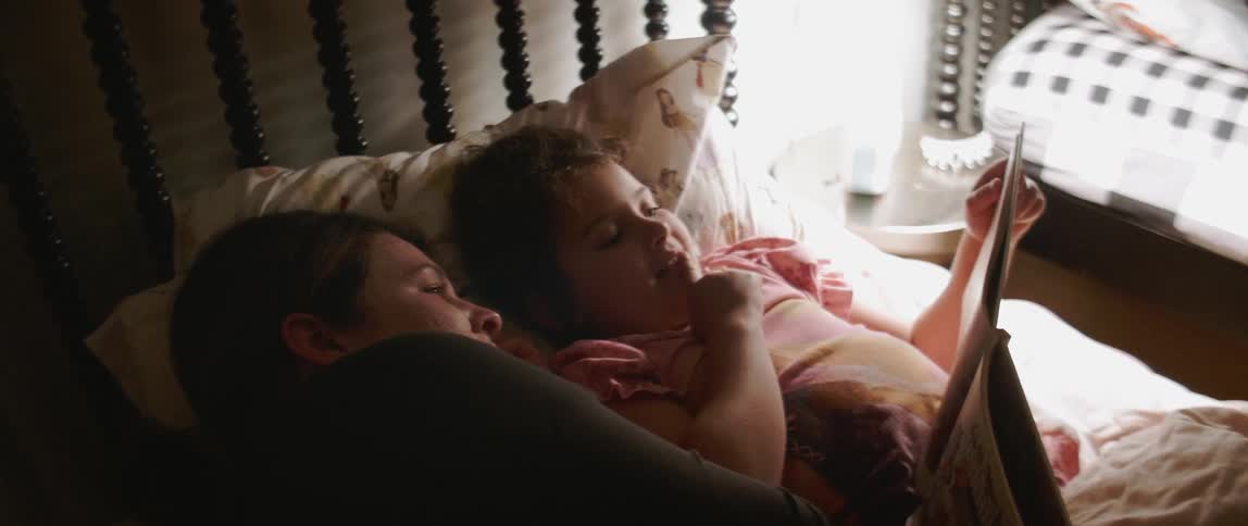 A woman and young girl read a book in bed