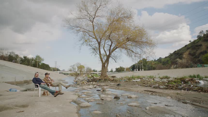Two people sit near a stream together
