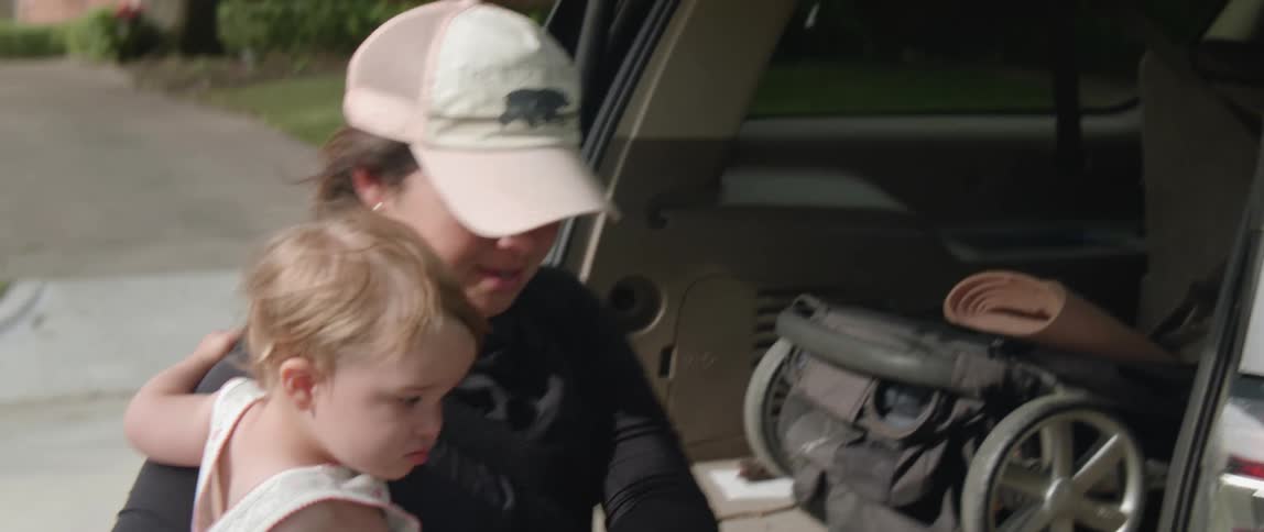 A woman unloads bags from a car while holding a baby