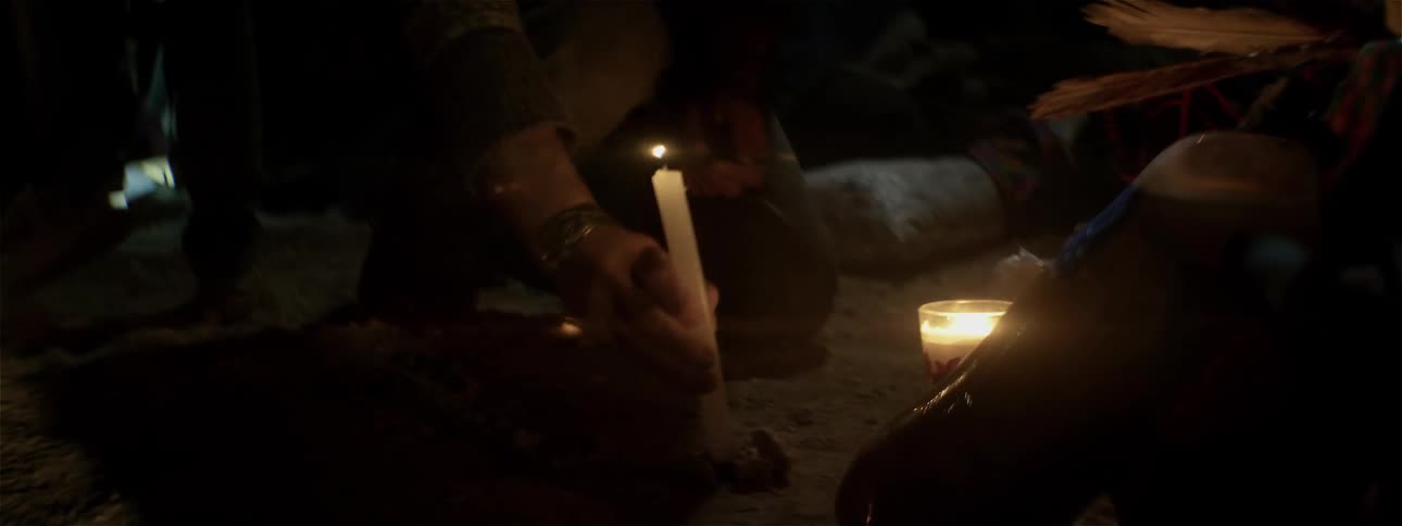 A person lights a candle and places it in the dirt
