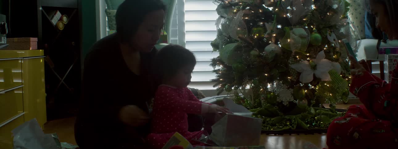 Woman and baby open a present next to a christmas tree