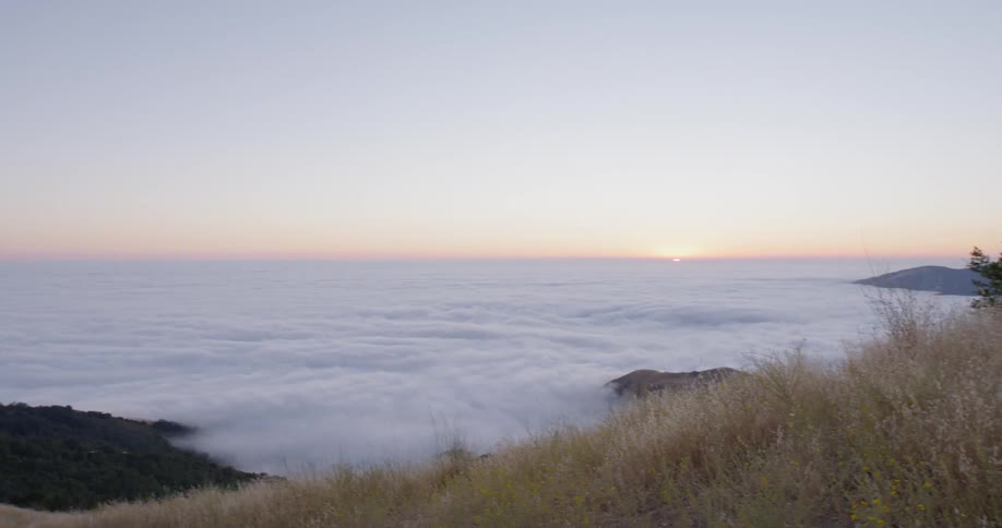 A grassy hilltop overlooks a valley covered by fog