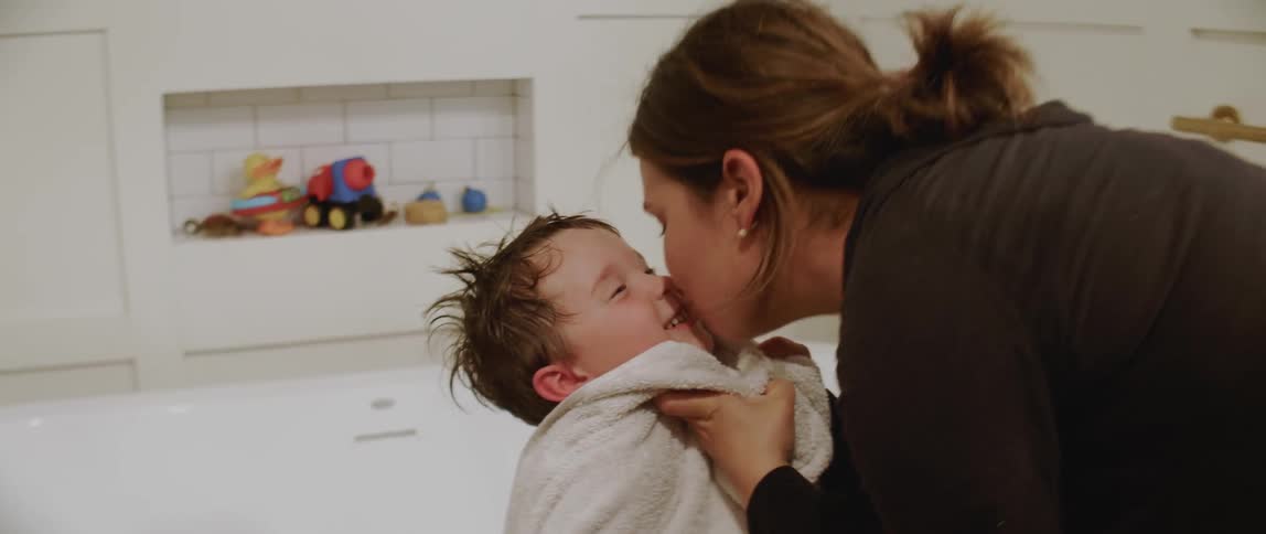 A mom kisses her child as she dries him off after a bath