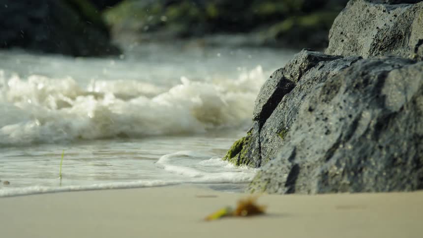 Water splashes up onto the beach and rocks