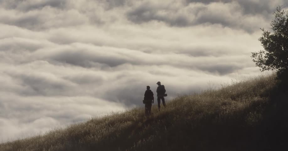 The two people stand on the high hill with heavy clouds behind them
