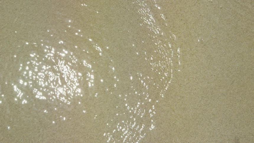 Sun reflects off water splashing over sand
