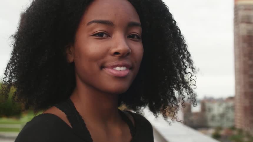 A woman is standing on a roof looking at the camera and smiles
