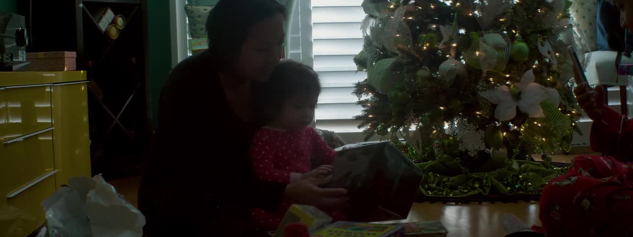 Child opening present with their parents while sitting next to the christmas tree