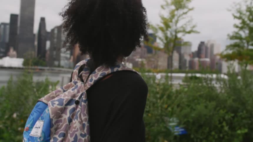 Woman walking by the water with a city across