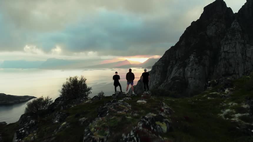 Three people stand on top of a cliff overlooking a lake