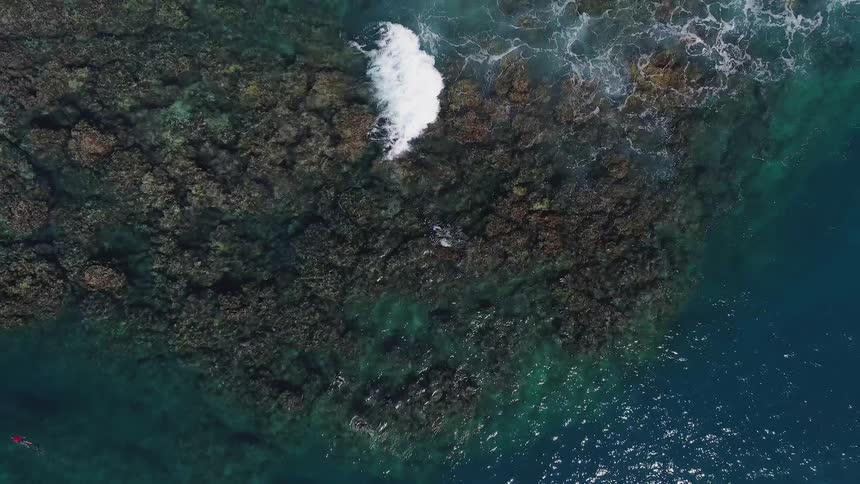 A blue ocean with waves crashing over a rocky island