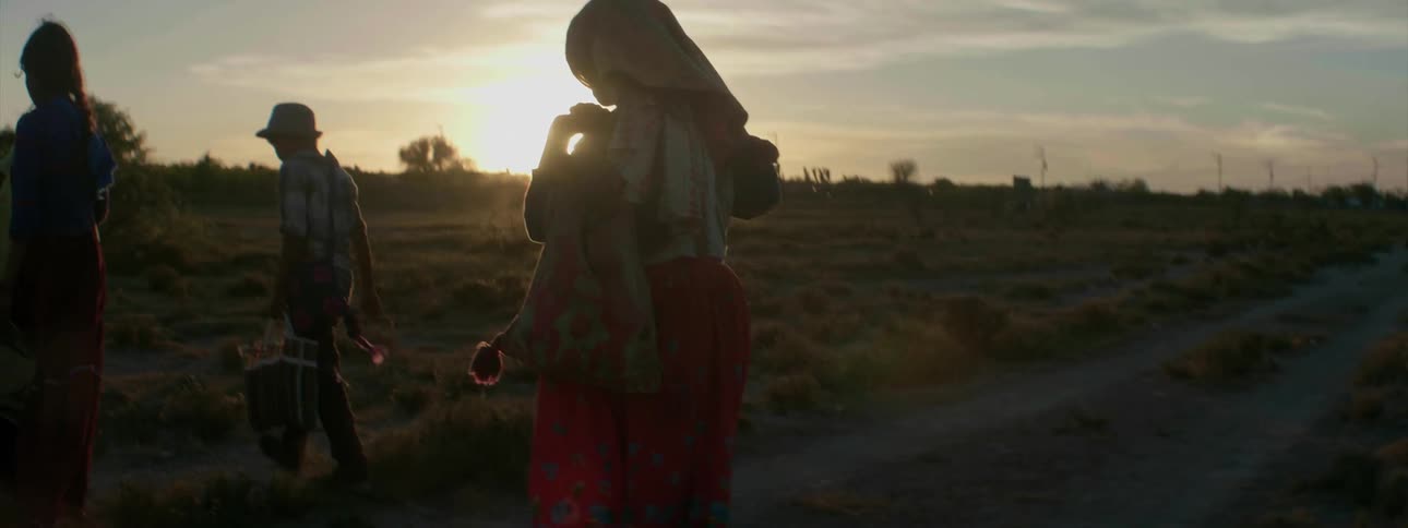 A man and a woman walking across a dirt road at sunset