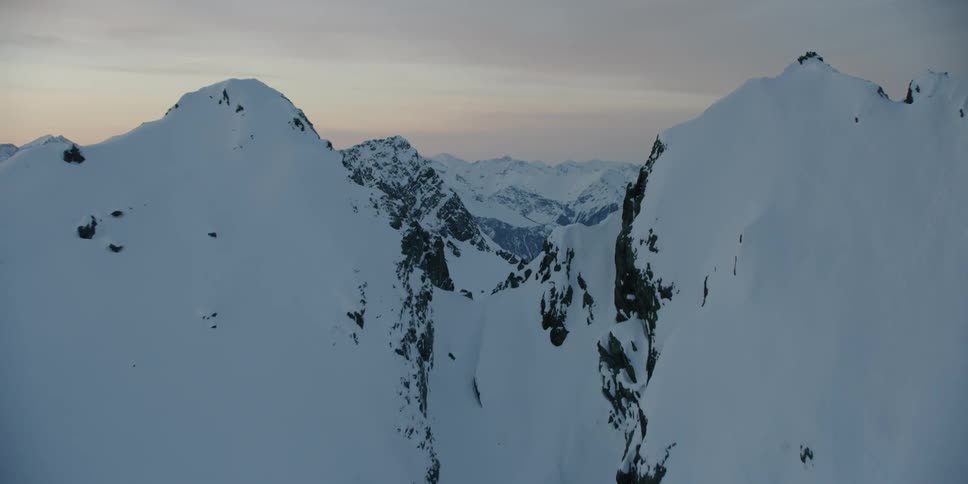 Many snow covered mountains at sunset with grey clouds in the sky