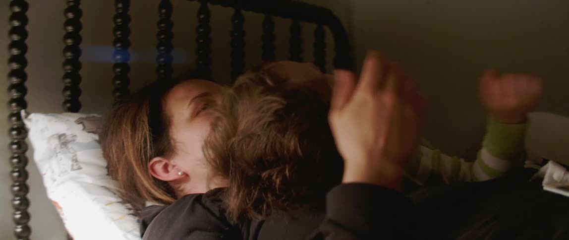 A mom cuddles and plays with her child in bed