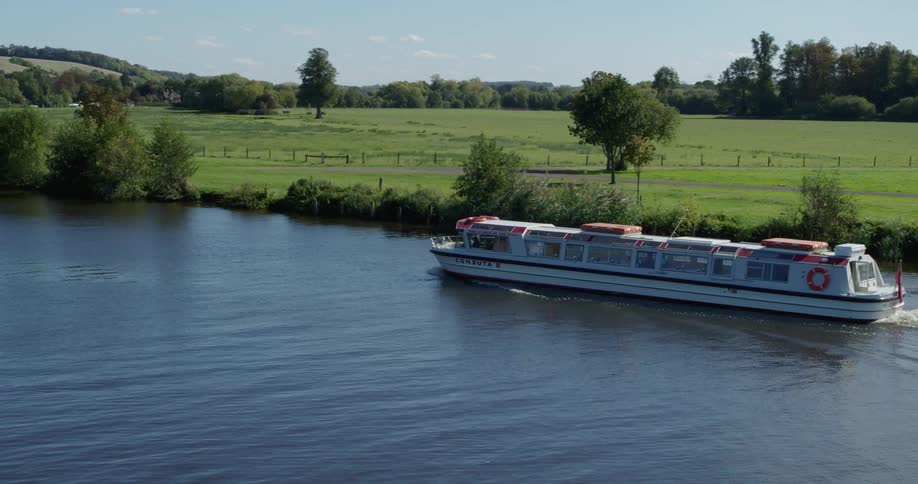 Long passenger boat moving swiftly down a river on a clear day