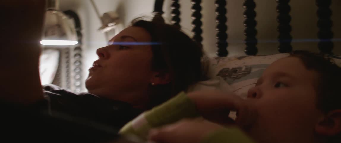 A mom lies in bed next to her child and reads a story
