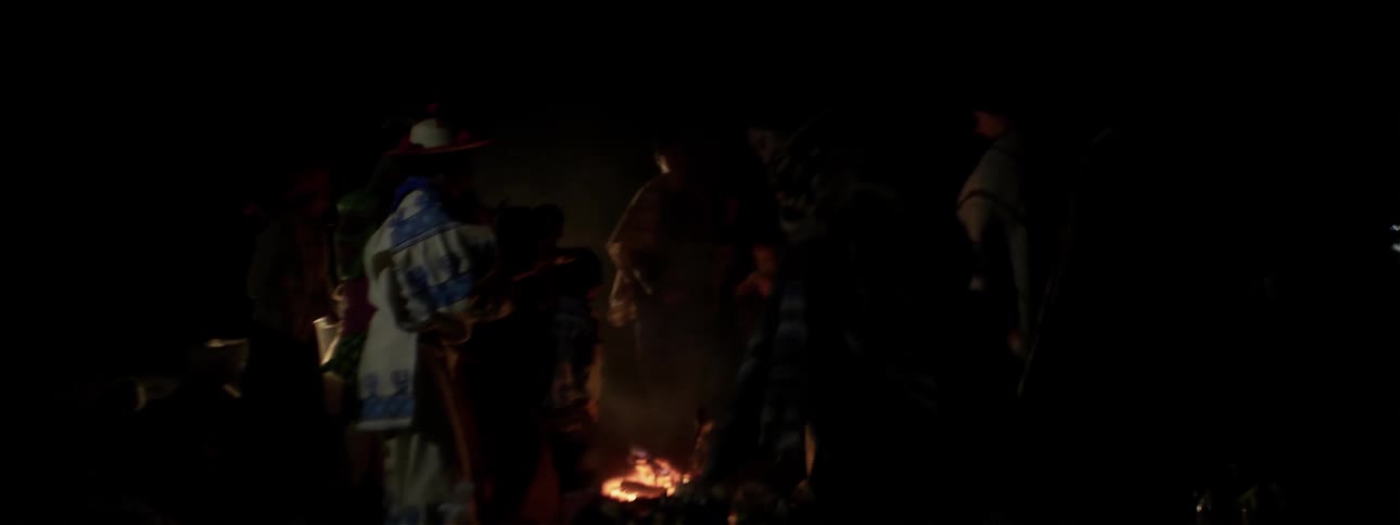 People dance around a campfire at night