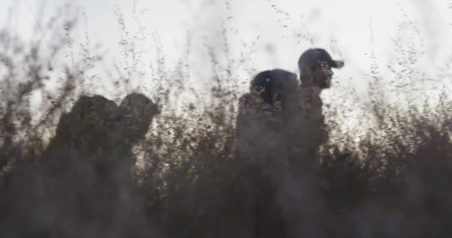 Two men hike through a field at sunset