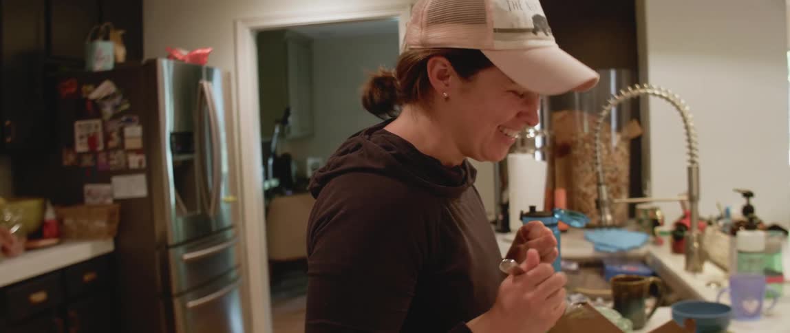 A woman smiles while eating takeout in a kitchen